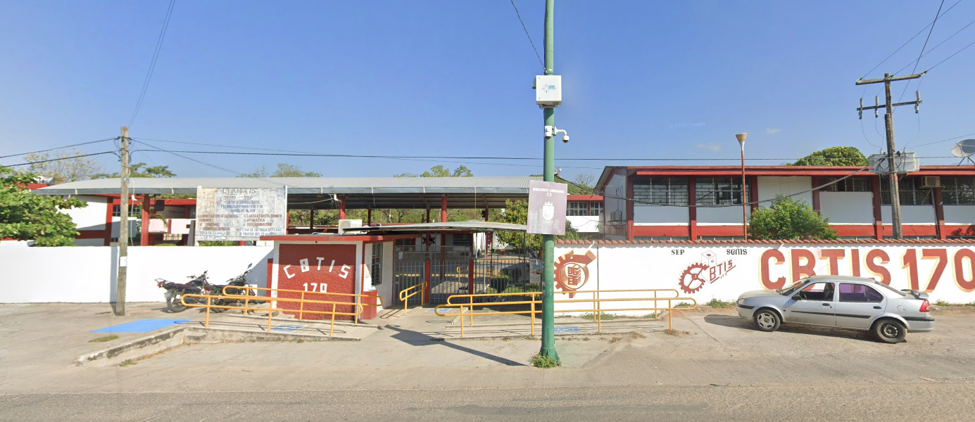 Fotografía en la que se muestra la entrada del plantel, conformada por una reja metálica y muros de color blanco que en letras grandes rojas dice Cebetis 170. Frente a la reja hay tres rampas con barandales de color amarillo.
